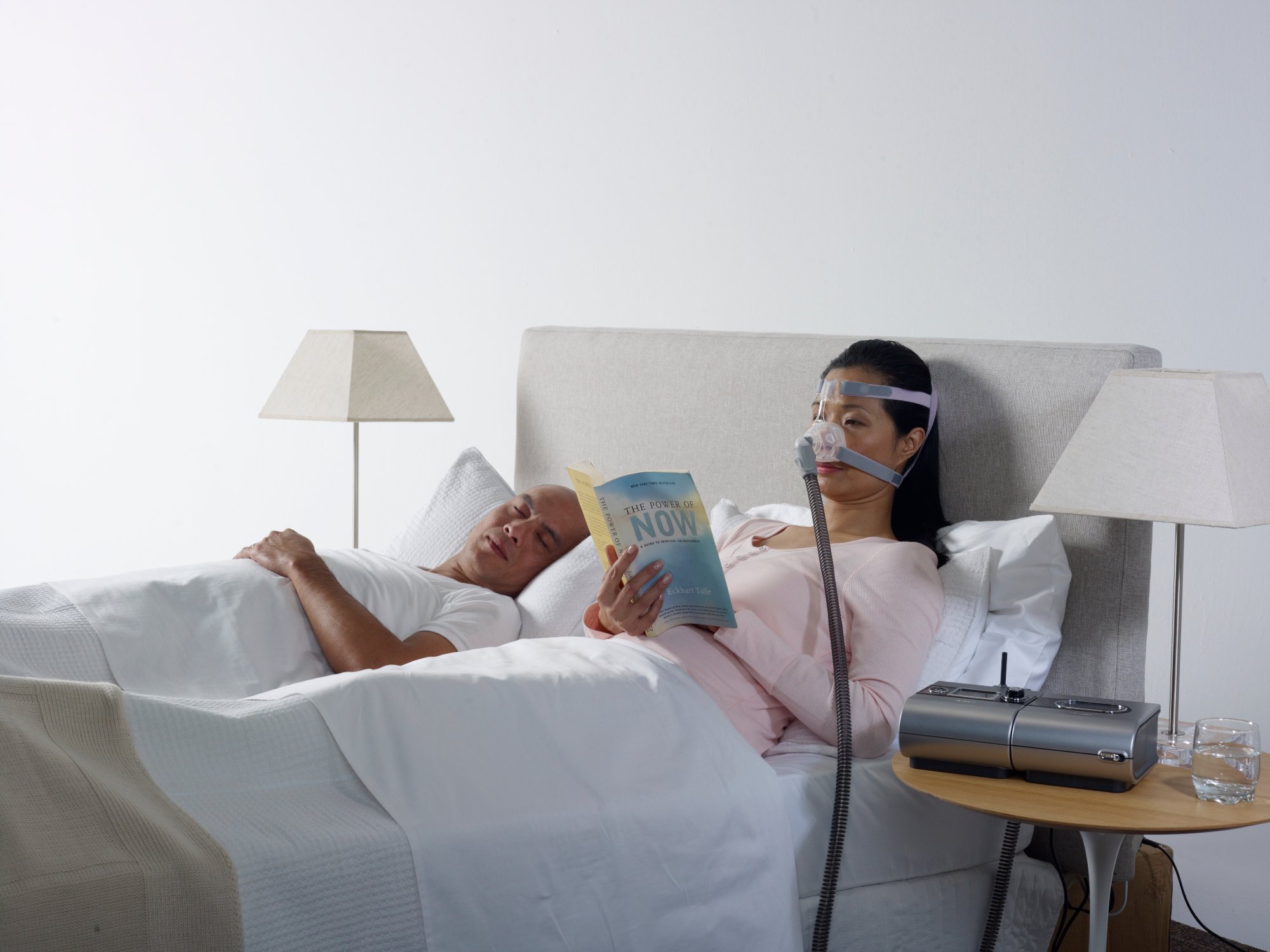 Woman and man in bed, woman is wearing cpap mask while reading her book